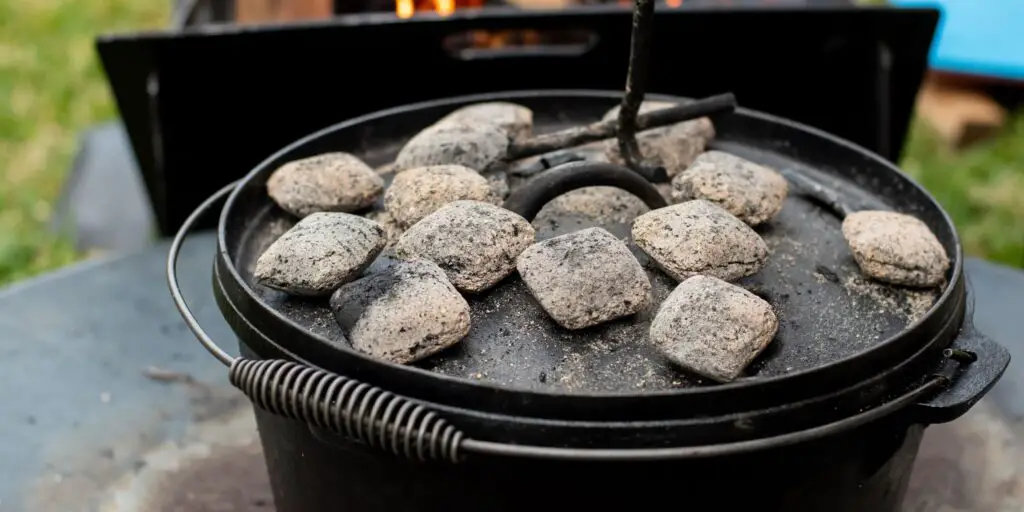 a picture of a camp dutch oven with coals on top of its lid